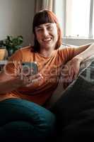 Take the day off and invite some friends over. an attractive young woman using her cellphone while relaxing on the sofa at home.