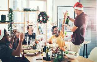 Its champagne time. a handsome young man popping champagne while dining with his friends at Christmas.