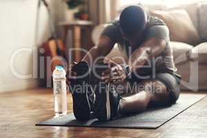 Keep pushing yourself to become the best. a sporty young man stretching his legs while exercising at home.