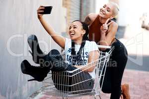 Were having fun out here. two cheerful young girlfriends taking a selfie while playing around with a shopping cart outdoors.