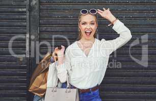 Guess what I bought today. Cropped portrait of an attractive young woman lifting her sunglasses while holding shopping bags against an urban background.