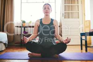 Aligning my chakras. an attractive young woman sitting on a yoga mat and meditating alone in her home.