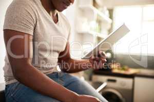 Lets see whats trending today. an unrecognizable man using a digital tablet while sitting on the kitchen counter at home.