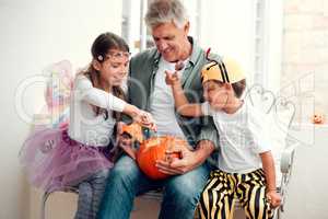 Were carving out some good times with grandad. two adorable young siblings carving out pumpkins for Halloween with their grandfather at home.