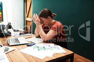This is so overwhelming. an attractive young businesswoman sitting alone at her desk and suffering from a headache.