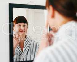 Your beautiful face deserves all the pampering it can get. an attractive young woman applying moisturizer on her face while standing in front of the mirror at home.