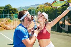 We trained hard for this trophy. two young sportspeople standing together and kissing a trophy after winning a tennis match.