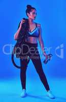 Shes always ready for a challenge. Full length shot of an attractive young sportswoman posing carrying battle ropes against a blue background.