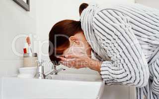 The mornings here and its time to freshen up. an unrecognizable woman washing her face in the bathroom sink at home.