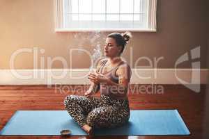 The smoke of palo santo sticks is so powerfully cleansing. a young woman burning a palo santo stick while sitting on a yoga mat at home.