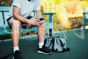 Connectivity on the courts. Closeup shot of an unrecognisable man using a cellphone while sitting on a bench on a tennis court.