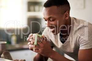 So much happiness in one cup. a handsome young man smiling while having a cup of coffee in his kitchen at home.