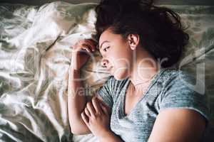 Wish life was a little kinder to me right now. High angle shot of an attractive young woman looking depressed while lying on her bed at home.