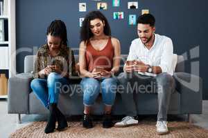 All in their own digital worlds. Full length shot of a diverse group of business colleagues sitting on a sofa together and using their cellphones.