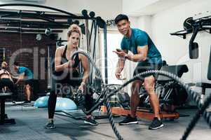 You can do this. an attractive young sportswoman working out with battle ropes with her personal trainer in a gym.