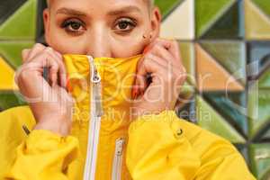 Playing hide and seek. Cropped portrait of an attractive young woman standing against a tiled wall and covering her mouth with her jacket.