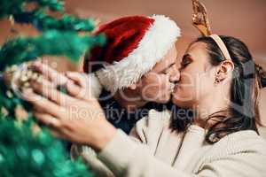 No mistletoe, no problme. an affectionate young couple decorating their Christmas tree together at home.