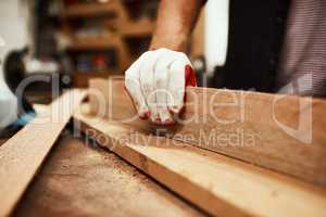 Almost done with you. Closeup of an unrecognizable male carpenter using sandpaper to smoothen out a piece of wood inside of a workshop at night.