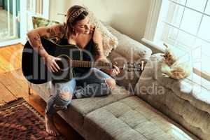 Some of the greatest hits were made at home. a young woman playing a guitar on a relaxing day at home.