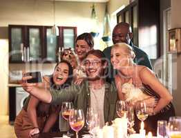 Time for a quick photo. a group of cheerful young friends taking a self portrait together with a cellphone during a dinner party at home.
