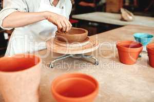 Its not just a bowl, its art. an unrecognizable woman shaping a clay pot in her workshop.