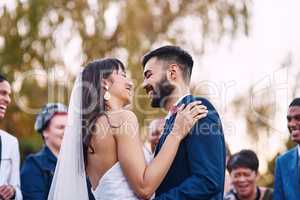 Sharing a moment called happy. an affectionate young newlywed couple smiling at each other on their wedding day with their guests in the background.
