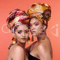 Wear your history and heritage with pride. Studio shot of two attractive young women wearing traditional African head wraps posing together against an orange background.