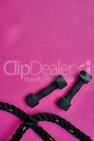 Who wants to get fit. High angle shot of two lightweight dumbbells and piece of rope placed on a pink background inside of a studio.