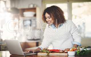 Happy woman following an online recipe, cooking healthy food on her home kitchen table or counter. Smiling African American female preparing fresh ingredients for a wellness lifestyle meal.