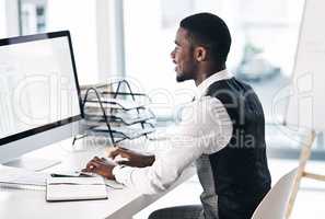 Success is a daily commitment. a young businessman using a computer at his desk in a modern office.