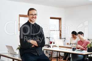 The way to predict the future is to create it. Cropped portrait of a handsome young businessman sitting with his arms folded while his colleagues works behind him.