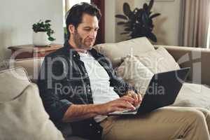 Weekends are meant for blogging. a handsome young man using his laptop while relaxing on a couch at home.