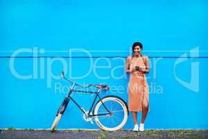 Ill be there in a few minutes guys. Full length shot of an attractive young woman using a cellphone while standing next to her bicycle doors.