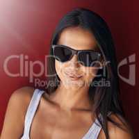 Cool, confident and beautiful woman wearing sunglasses and smiling against a red wall with lens flare. Face of a cheerful, stunning and happy female feeling good and showing a positive attitude