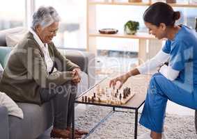 Playing games are a great way to keep the mind active. a young nurse playing chess with a senior woman in a retirement home.