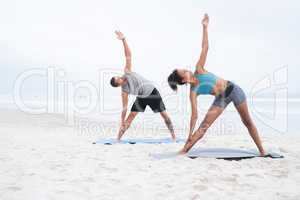 Yoga lies at the core of their wellbeing. a young man and woman practising yoga together at the beach.
