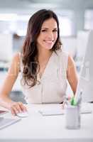 Smiling, confident and young female business worker sitting at a office computer. Portrait of a market research consultant doing advertising. Beautiful woman employee feeling positive about marketing