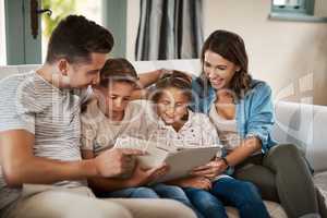 Technology connects us with family in more ways than one. a young family of four reading a book together on the sofa at home.