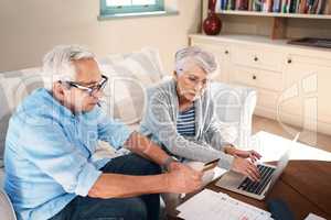 Settling their bills with the convenience of credit. a senior couple using a credit card while going through paperwork at home.