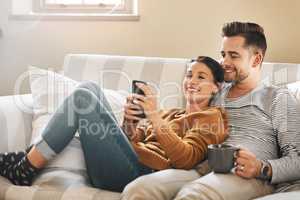 Should we call and hear if they want to come over. a young couple using a cellphone while relaxing on the sofa at home.