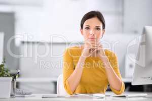 Serious, confident and ambitious business woman sitting at her desk while resting her chin on her hands. Portrait of a female entrepreneur showing great leadership skills while working in an office