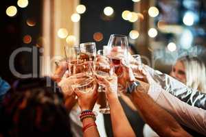 Drinks all around. a group of unrecognizable friends having a celebratory toast with their drinks inside of a bar at night.