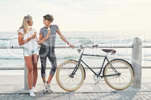 Sharing some gossip over ice cream. two friends eating ice cream while standing on the promenade with a bicycle.