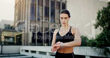 Keeping her fitness levels right on track. a young woman looking at her watch while exercising in the city.