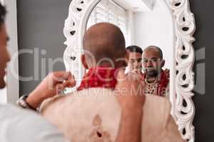 Almost done with the look. a young best man helping the groom with getting dressed while standing in front of the mirror on the wedding day.