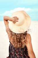 Hats on and shoes off. Rearview shot of a young woman spending the day at the beach.