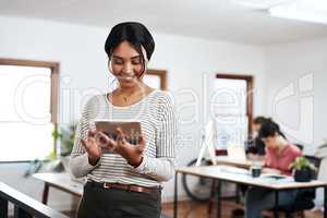 Updating my tasks for the day. an attractive young businesswoman using a tablet while her colleagues work behind her in the office.
