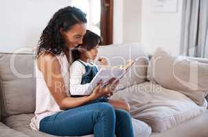 Bonding time involves reading our favorite books. a young girl reading a book while sitting with her mother at home.