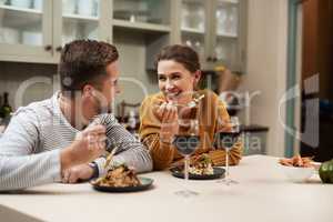 Date nights keep their spark alive. an affectionate young couple smiling at each other while enjoying dinner in their kitchen at home.