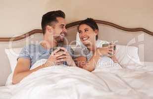 Were staying in today. a happy young couple drinking coffee in bed in their bedroom at home.